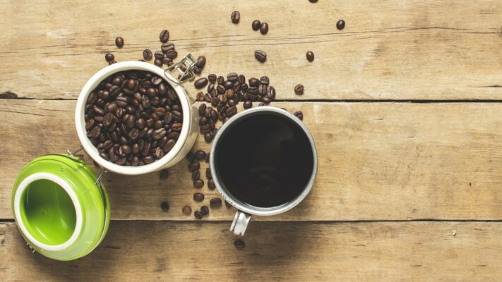befüllte Dose zur Kaffeeaufbewahrung mit Kaffeetasse auf Holzboden